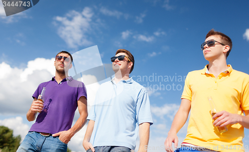 Image of happy friends drinking beer and walking on beach