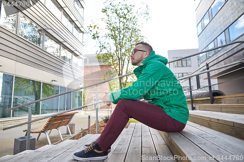 Image of happy young hipster man sitting on stairs in city