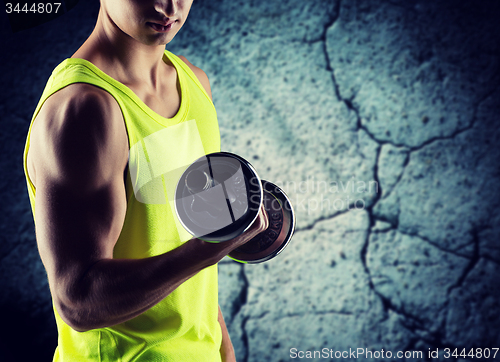 Image of close up of young man with dumbbell flexing biceps