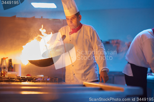 Image of chef in hotel kitchen prepare food with fire