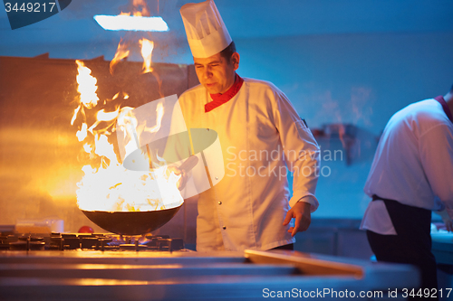 Image of chef in hotel kitchen prepare food with fire