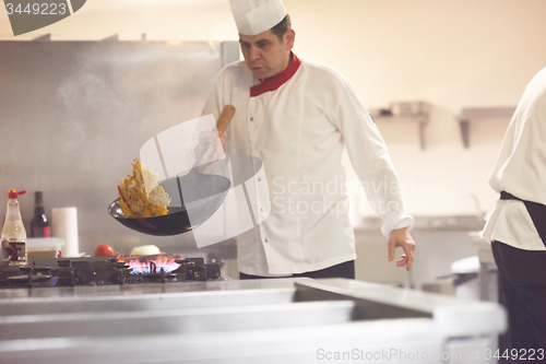 Image of chef in hotel kitchen prepare food with fire