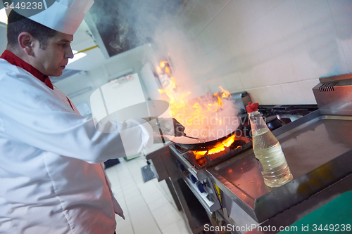 Image of chef in hotel kitchen prepare food with fire