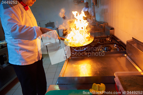 Image of chef in hotel kitchen prepare food with fire