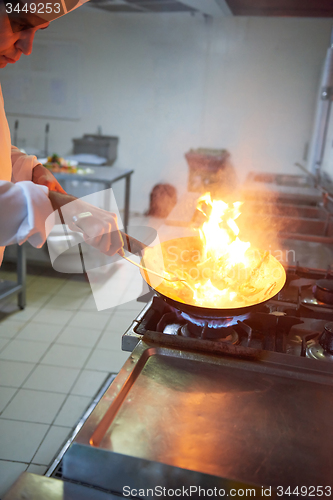 Image of chef in hotel kitchen prepare food with fire