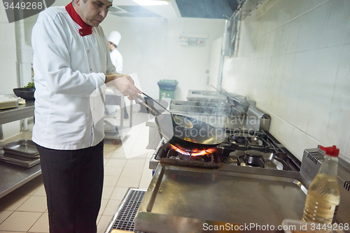 Image of chef in hotel kitchen prepare food with fire