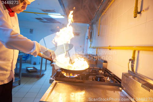 Image of chef in hotel kitchen prepare food with fire