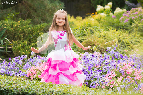 Image of Happy little girl in a pink dress at flower bed