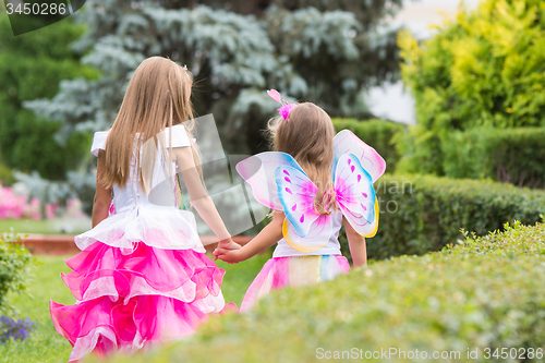 Image of Two little girls, princess and fairy, walk hands in the garden