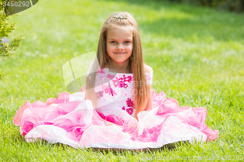 Image of Five-year girl in a beautiful dress sat on the lawn in the green garden