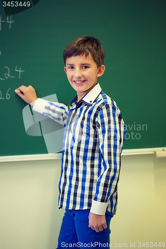 Image of little smiling schoolboy writing on chalk board