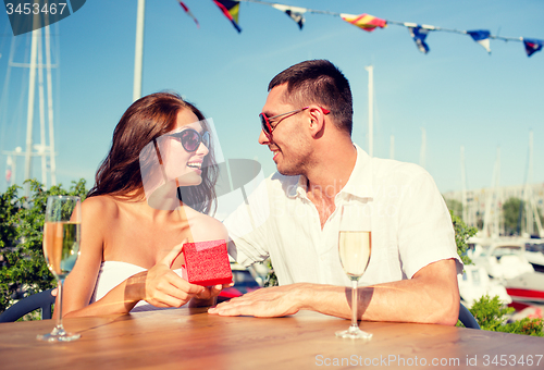 Image of smiling couple with champagne and gift at cafe