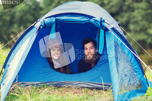 Image of smiling couple of tourists looking out from tent