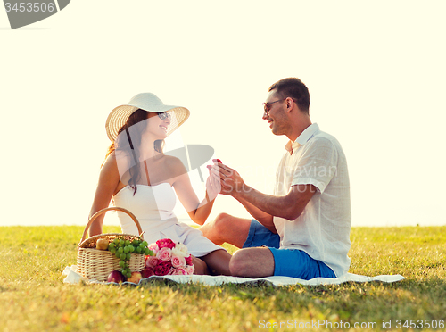 Image of smiling couple with small red gift box on picnic