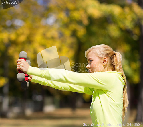 Image of sporty woman with light dumbbells outdoors