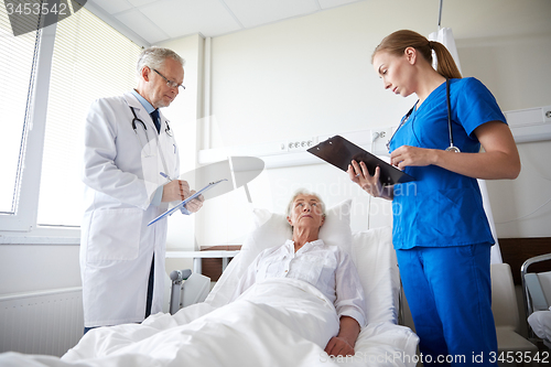 Image of doctor and nurse visiting senior woman at hospital