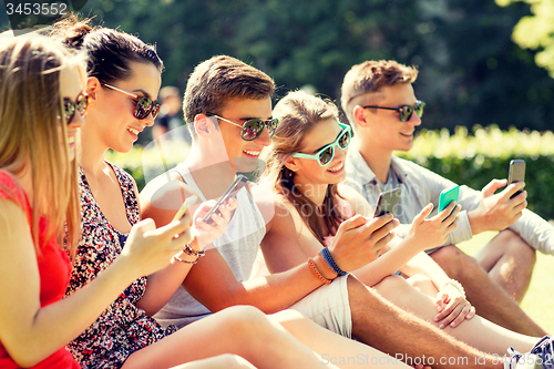 Image of smiling friends with smartphones sitting on grass