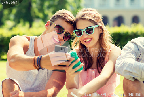 Image of smiling friends with smartphones sitting in park