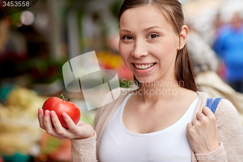 Image of happy woman holding tomato at street market