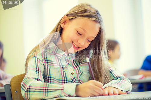 Image of smiling school girl writing test in classroom