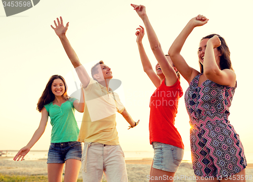 Image of smiling friends dancing on summer beach