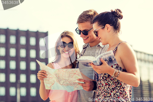 Image of smiling friends with map and city guide outdoors