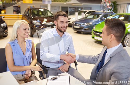 Image of happy couple with car dealer in auto show or salon