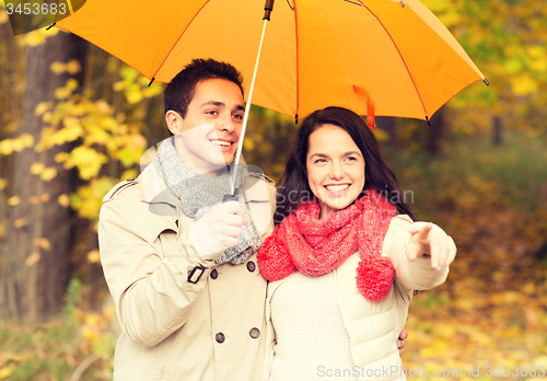 Image of smiling couple with umbrella in autumn park