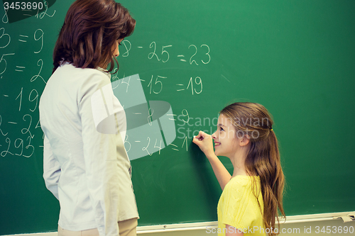 Image of little smiling schoolgirl writing on chalk board