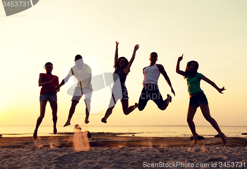 Image of smiling friends dancing and jumping on beach