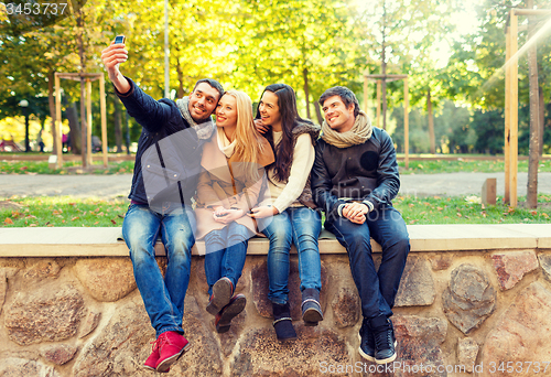 Image of smiling friends with smartphones in city park