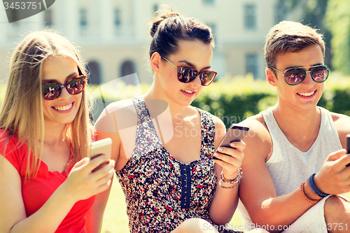 Image of smiling friends with smartphones sitting on grass