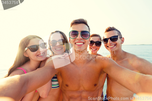 Image of group of smiling friends making selfie on beach