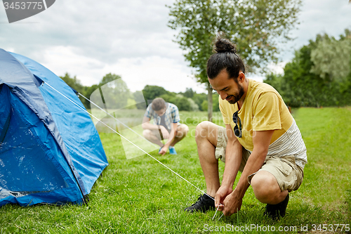 Image of smiling friends setting up tent outdoors