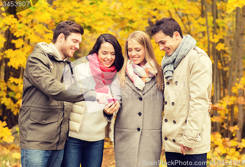 Image of smiling friends with smartphones in city park