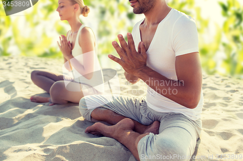 Image of smiling couple making yoga exercises outdoors