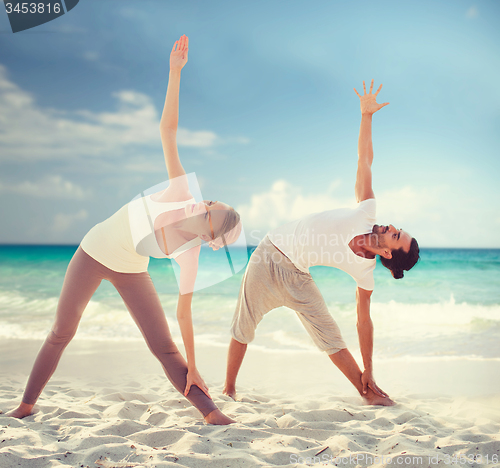 Image of couple making yoga exercises on summer beach