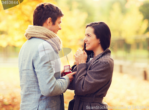 Image of smiling couple with red gift box in autumn park