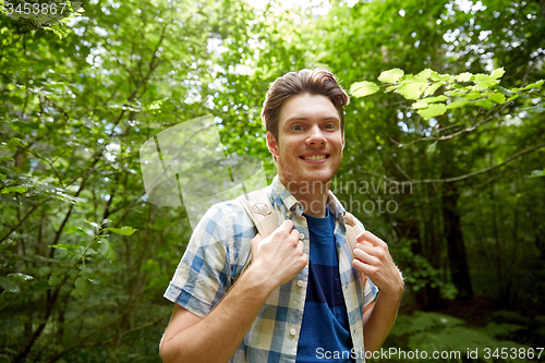 Image of smiling young man with backpack hiking in woods