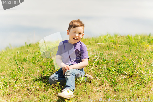 Image of happy little boy sitting on grass outdoors