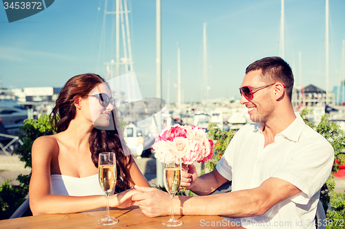 Image of smiling couple with bunch and champagne at cafe