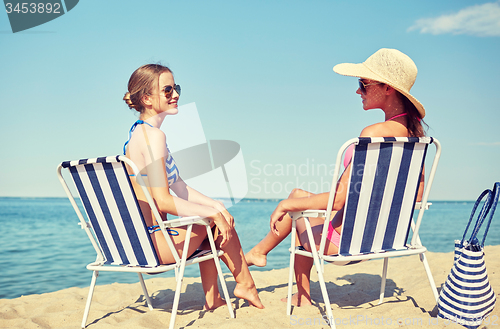 Image of happy women sunbathing in lounges on beach