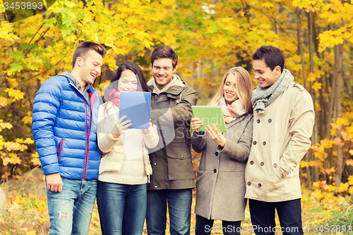 Image of group of smiling friends with tablets in park