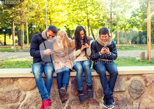 Image of smiling friends with smartphones in city park