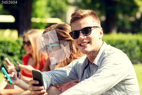 Image of smiling friends with smartphones sitting in park