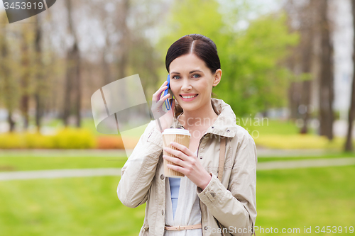 Image of smiling woman with smartphone and coffee in park