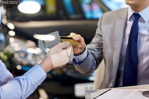 Image of customer giving credit card to car dealer in salon