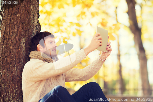 Image of smiling young man with tablet pc in autumn park