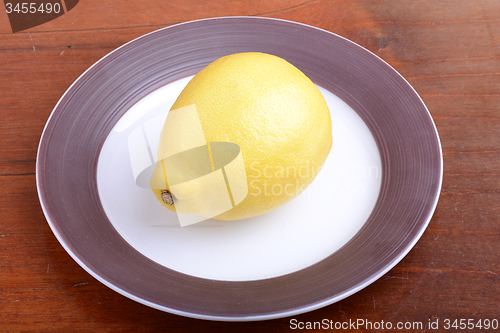 Image of Whole lemon on a grey plate on wooden background
