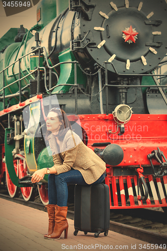 Image of pretty woman sitting on a suitcase on railroad station